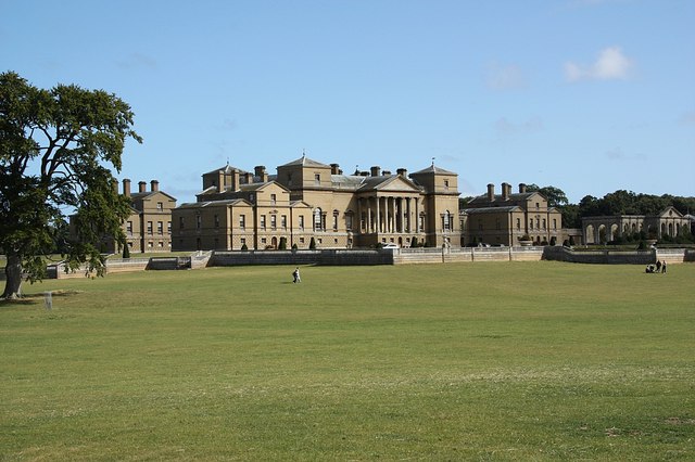 Holkham Hall: A large estate shown from far away. The lawn can be seen before the house as well. 