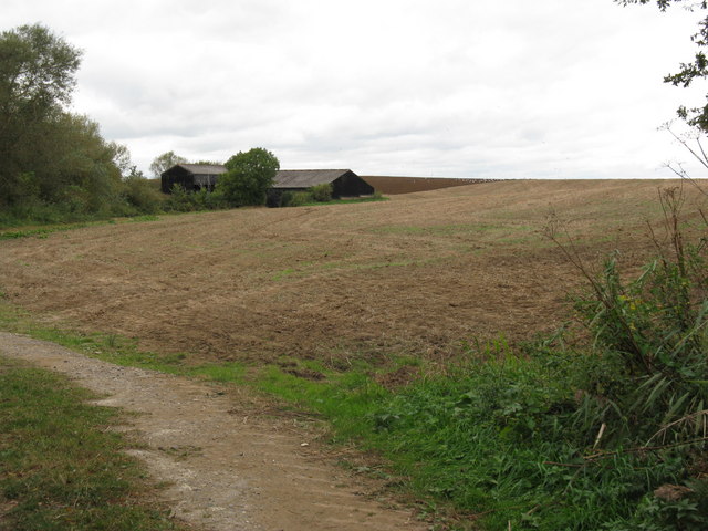 Part ploughed field next to black farm buildings