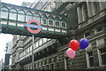 TQ3080 : View of the Charing Cross station footbridge, roundel and three balloons being carried by a zombie from Villiers Street by Robert Lamb