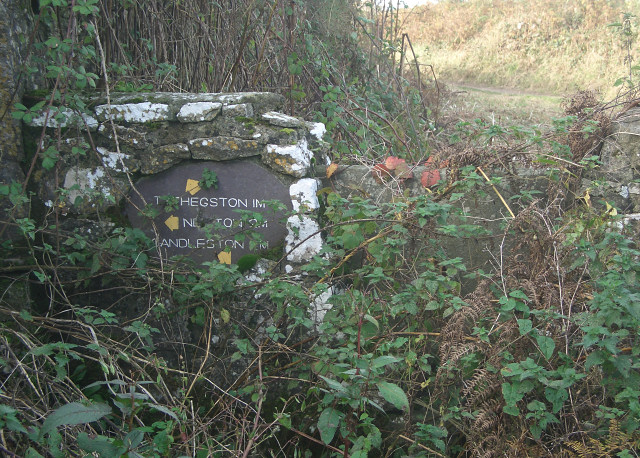 Overgrown stone sign and stile by Candleston