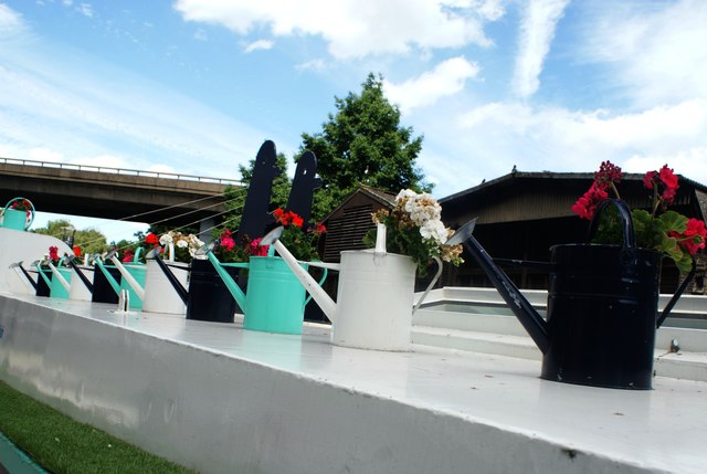 View of a row of watering cans with flowers in on top of a boat near the Paddington Basin