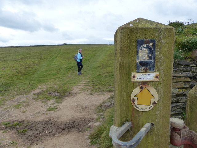 Coast path walker and marker on a gate post