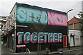 View of a "Stronger Together" mural on the side of N B Patel Newsagents on Lea Bridge Road from Sanderstead Road