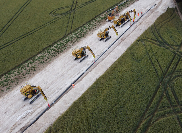Five excavators lowering pipeline into trench