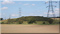 Pylons dwarf the low hillside beyond the flat ploughed field